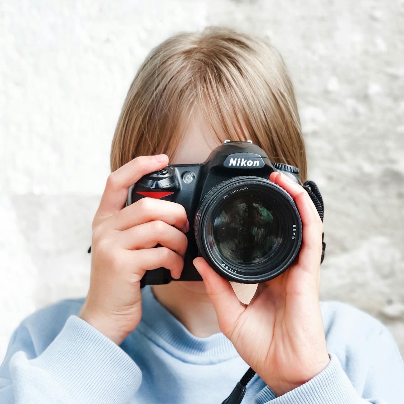 a young girl in blue sweater holding a black sony dslr camera